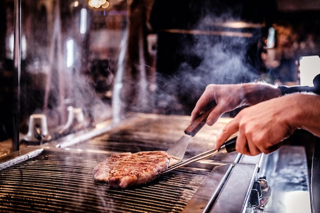 Master chef wearing uniform cooking delicious beef steak on a kitchen in a restaurant