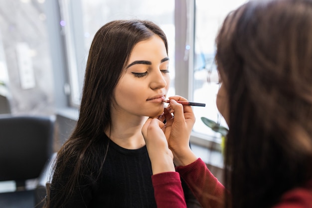 Master is painting lips of pretty young model before photosession