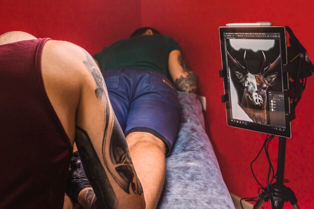 Master making tattoo in studio with screen with draft