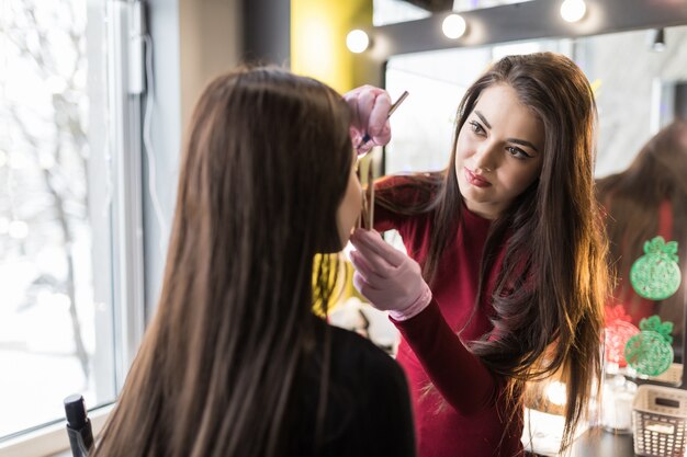 Master in white gloves doing professional make up of young woman