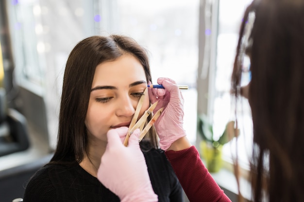Master in white gloves work at balck eyebrows technique in beauty salon