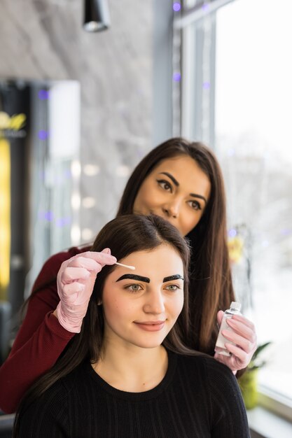 Master in white gloves work at balck eyebrows technique in beauty salon