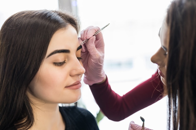 Master in white gloves work at balck eyebrows technique in beauty salon