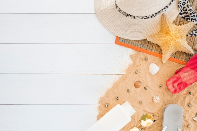 Mat with hat and starfish near seashells and lotion on sand