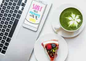 Free photo matcha green tea latte cup; cheesecake and mobile phone with morning message on an open laptop on white desk