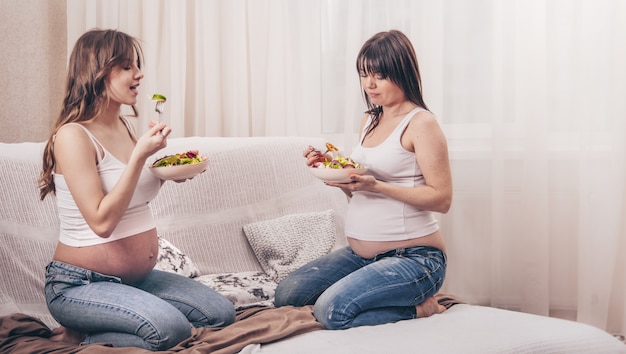 Maternity concept, two pregnant women eating fresh salad at home