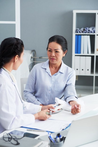 Mature Asian woman sitting in doctor's office and having blood pressure measured