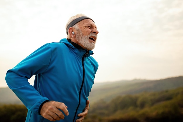 Mature athletic man getting out of breath while feeling pain during morning run in nature