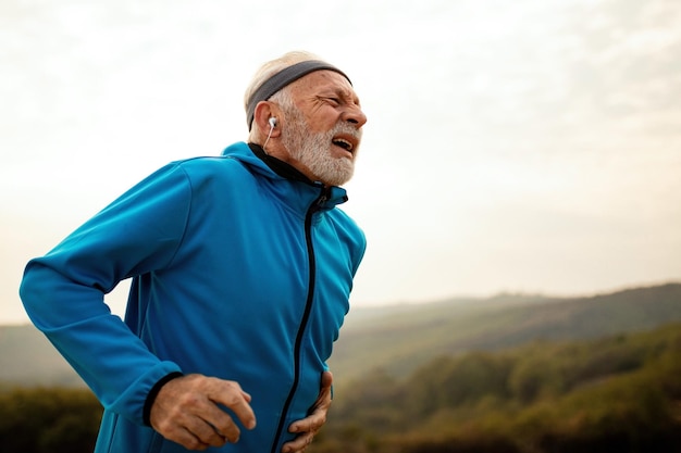 Зрелый спортивный мужчина задыхается, чувствуя боль во время утренней пробежки на природе