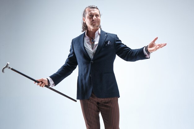 The mature barded man in a suit holding cane.
