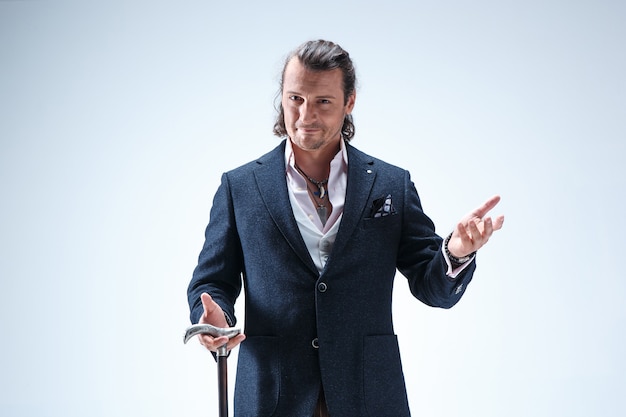 The mature bearded man in a suit holding cane. Isolated on a blue studio background.