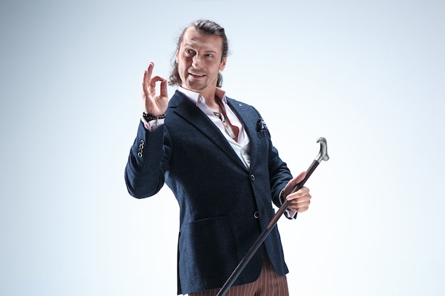 The mature bearded man in a suit holding cane. Isolated on a blue studio background.