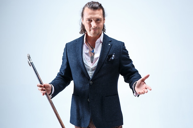 The mature bearded man in a suit holding cane. Isolated on a blue studio.