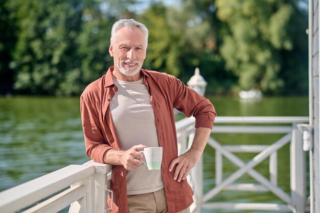 A mature bearded man with a cup in hands