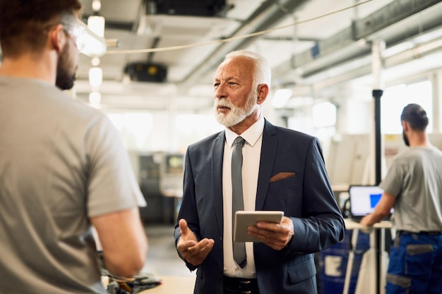 Mature businessman communicating with factory worker while visiting industrial facility