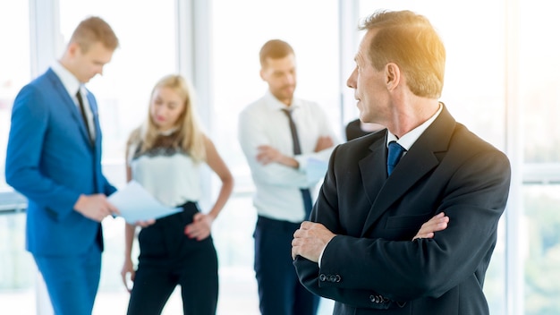 Free photo mature businessman with folded arms looking at his colleagues in office