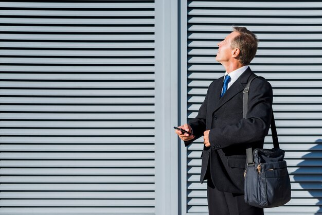 Mature businessman with mobile phone looking up