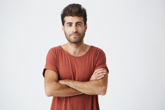 Mature caucasian student gently smiling, crossing hands and confidently  shooting for article about his start-up project. Man in red tshirt feeling proud and successful