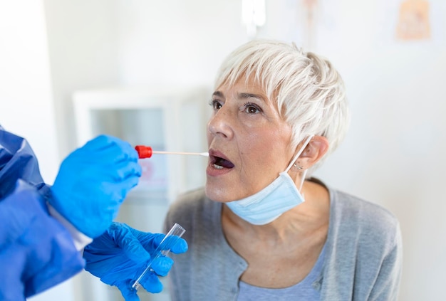 Mature Caucasian woman in a clinical setting being swabbed by a healthcare worker in protective garb to determine if she has contracted the coronavirus or COVID19