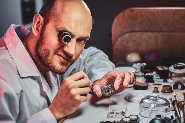 Mature clockmaster is fixing old watch for a customer at his busy repairing workshop.