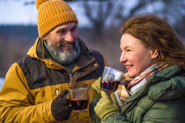 Mature couple enjoying mulled wine in winter romantic tour camping adventure Romantic mature couple family outreach with hot wine near camper Family adventure and vacation concept