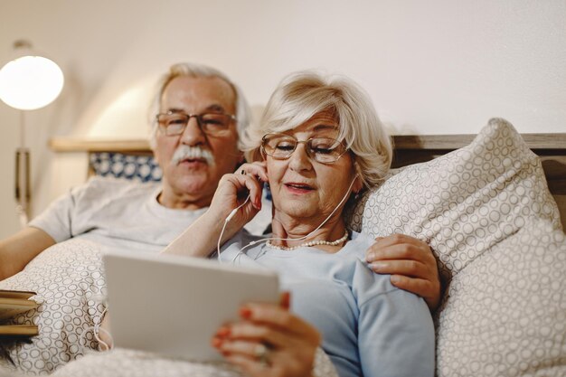 Mature couple relaxing in bed and using digital tablet Focus is on woman