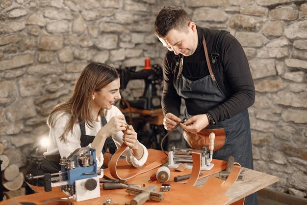 Mature craftsman with young woman working in workspace Man and woman wearing an apron and making a belt Grounge dark stone texture background