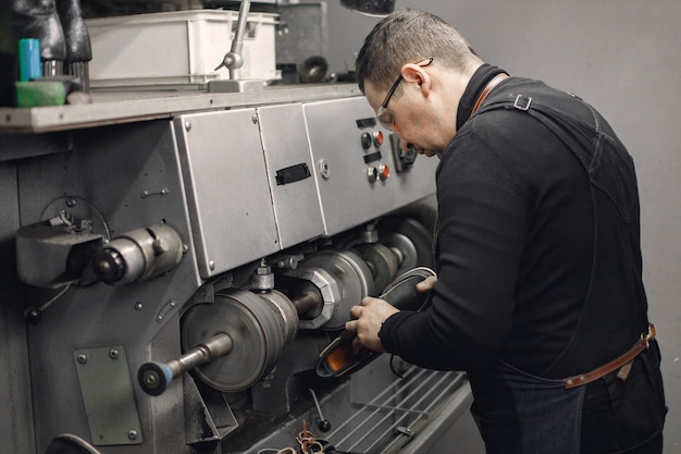 Artigiano maturo che lavora nel suo spazio di lavoro uomo che indossa un grembiule e utilizza una macchina speciale uomo che indossa un occhiali da vista