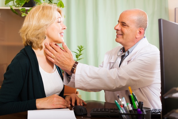 Foto gratuita medico maturo che controlla tiroide della donna sorridente