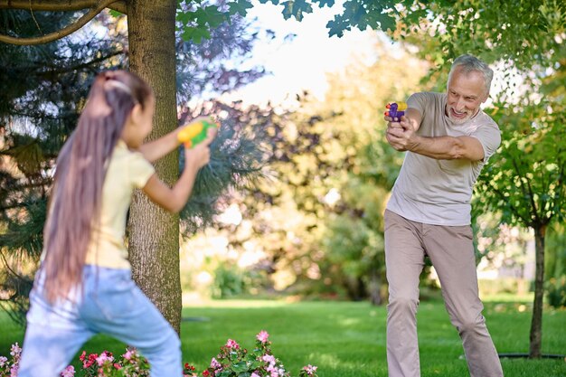 Mature gray-haired man playing paintball with a girl