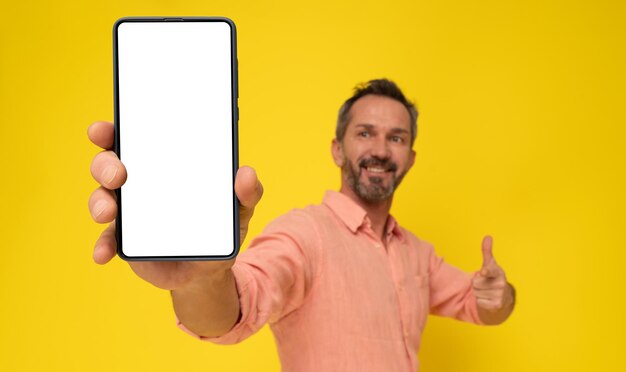 Mature grey haired man showing huge smartphone in hand happy smiling looking at device Mature fit man with phone app advertisement Selective focus on phone