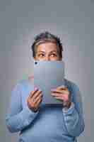 Free photo mature grey haired woman hide face smiling shy behind smartphone or modern gadget working or shopping online or checking on social media pretty woman in blue blouse isolated on yellow background