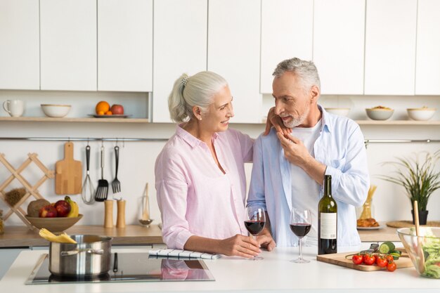 成熟した幸せな愛情のあるカップルがワインを飲んでキッチンに立っています。