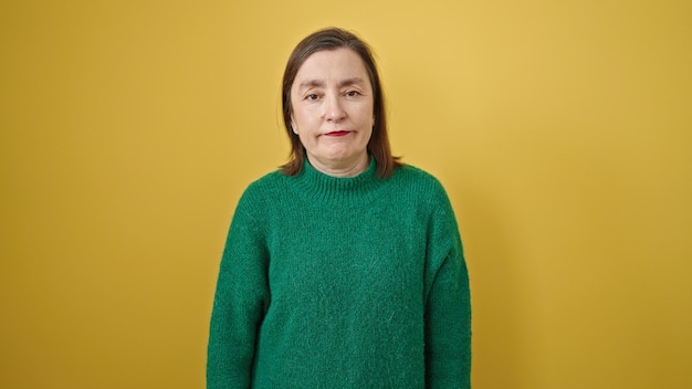 Mature hispanic woman with grey hair standing with serious expression over isolated yellow background