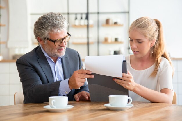 Mature legal advisor reading document and explaining details to young customer