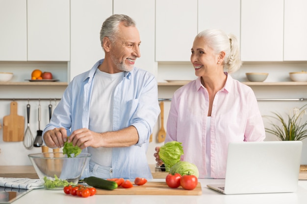 Mature loving couple family using laptop and cooking salad