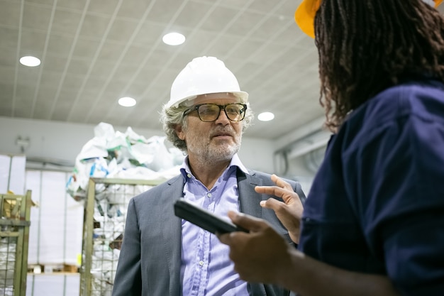 Mature male factory engineer and female worker talking on plant floor at control board of machine