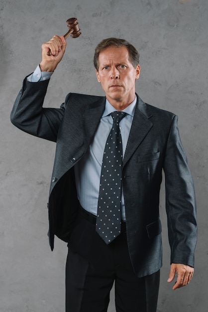 Free photo mature male lawyer hitting with gavel against gray textured background