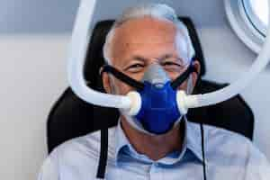 Free photo mature male patient wearing oxygen mask during hyperbaric oxygen therapy and looking at camera