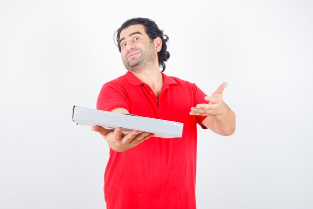 Mature male presenting pizza box in red t-shirt and looking cute , front view.