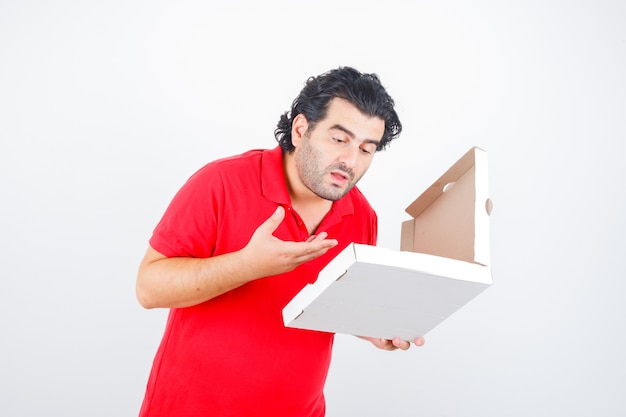 Mature male in red t-shirt looking at opened pizza box and looking hungry , front view.