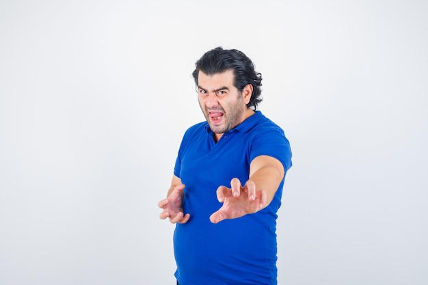 Зрелый мужчина в синей футболке, стоя в позе боя и глядя сердитый, вид спереди.