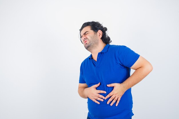 腹痛に苦しんでいる青いTシャツの成熟した男と痛みを伴う、正面図。