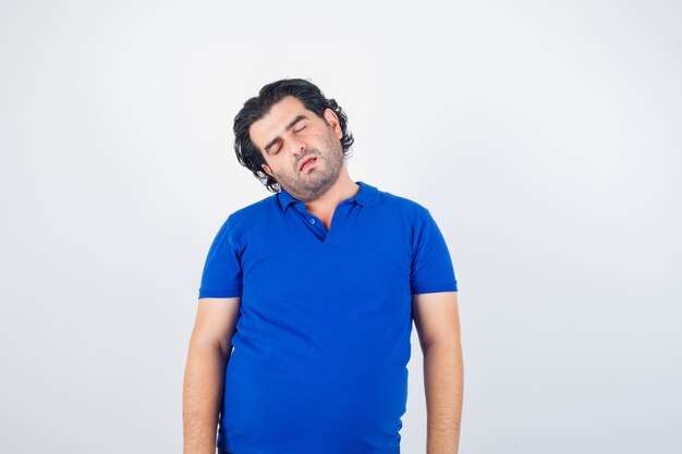 Mature man bowing head on shoulder in blue t-shirt and looking sleepy , front view.