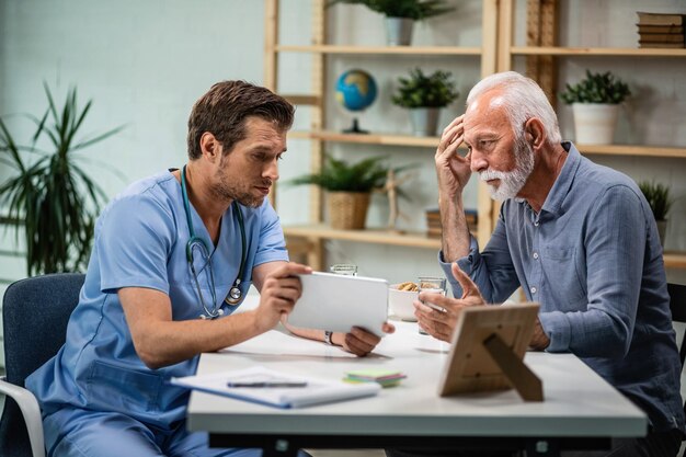 Mature man feeling concerned while talking to his doctor who is showing him medical test results on digital tablet