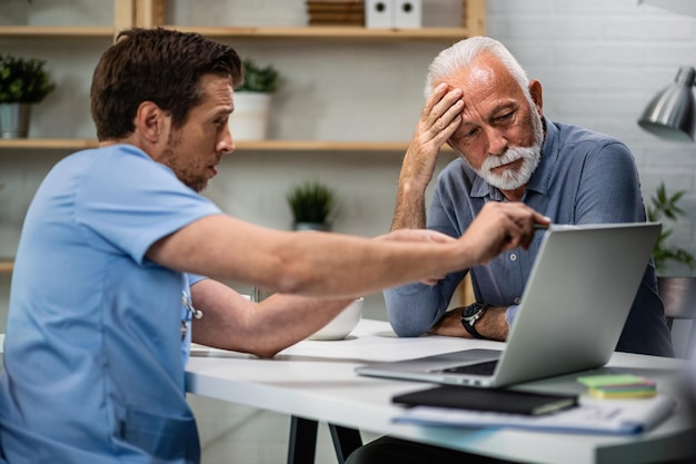 Зрелый мужчина чувствует беспокойство, используя компьютер со своим врачом, который объясняет результаты медицинских анализов после осмотра