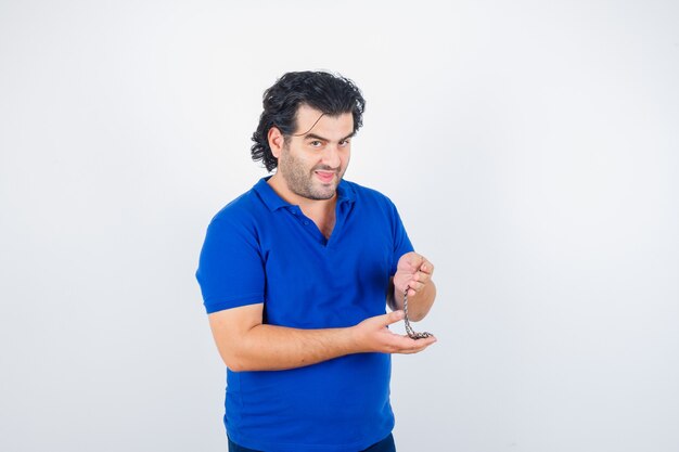 Зрелый мужчина держит цепь в голубой футболке и задумчиво смотрит, вид спереди.