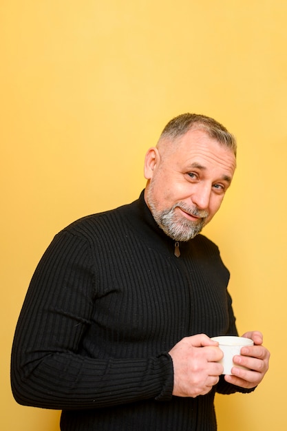 Mature man holding a cup of coffee next to a yellow wall