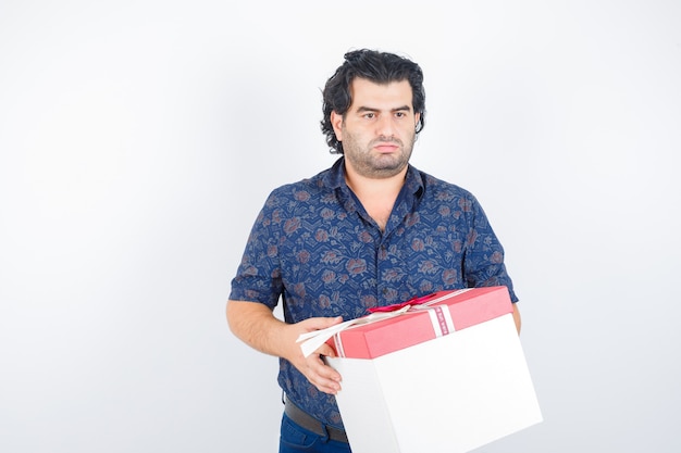 Mature man holding gift box while looking away in shirt and looking thoughtful. front view.