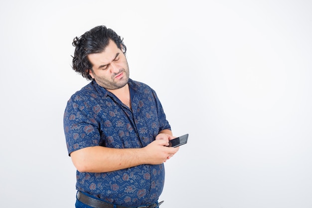 Mature man looking at mobile phone in shirt and looking pensive , front view.